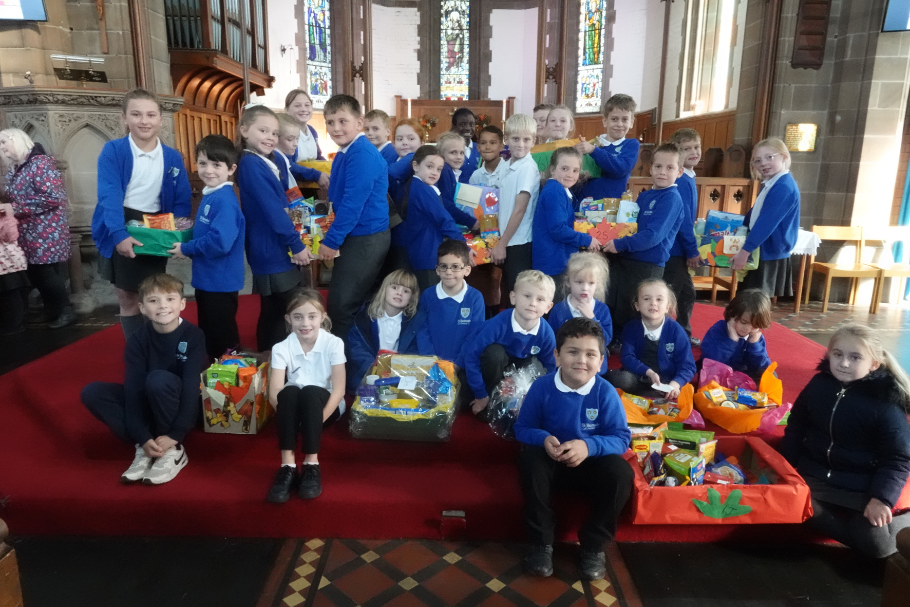 Children in front of the altar at St Barnabas Church with boxes full of harvest gifts