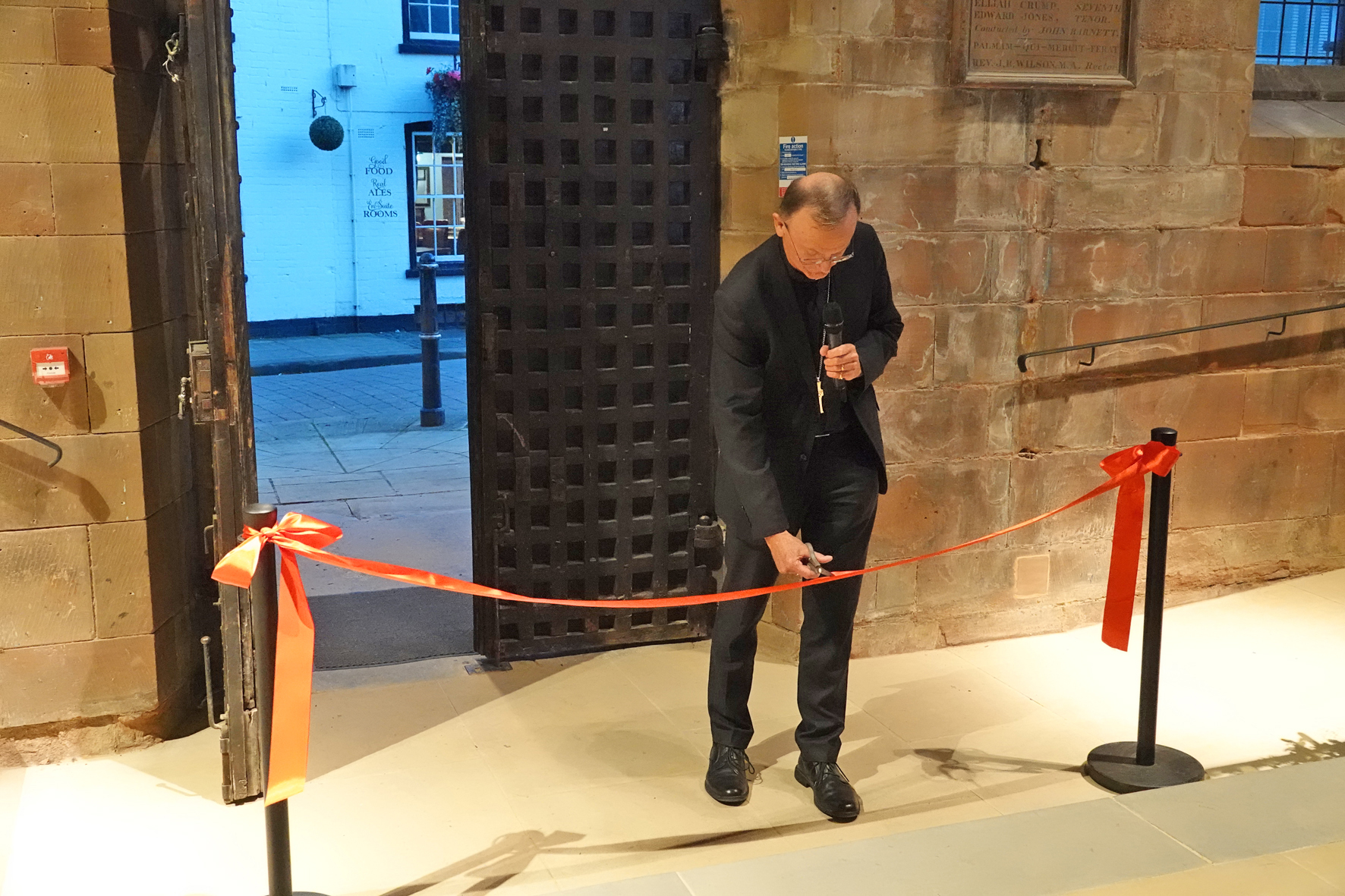 Bishop John cuts a red ribbon by the door of St Helen's Church