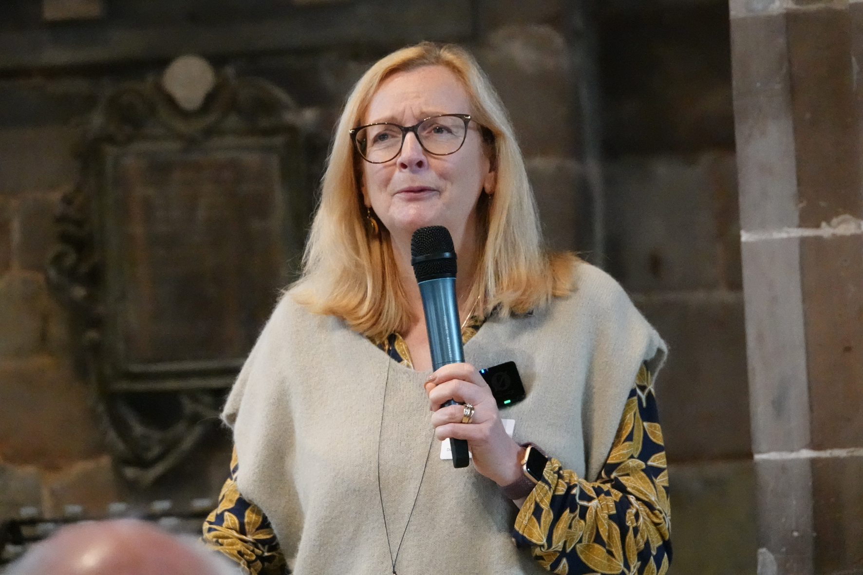 Sue Steer holding a microphone and standing presenting to people