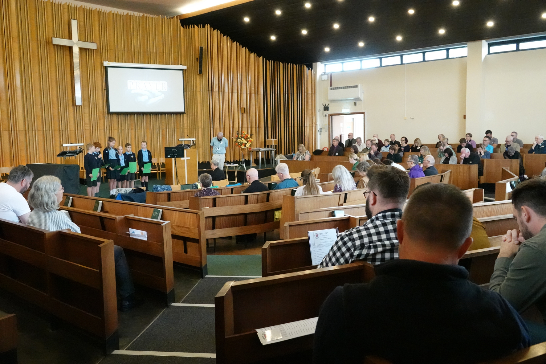 A view from the back of the clergy teaching morning with clergy sat around the room and some children and Duncan on the stage at the front