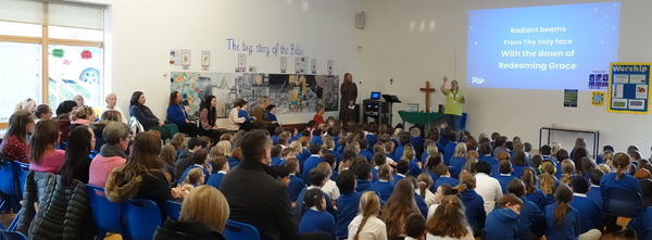 School hall filled with children and parents sat on chairs at the back