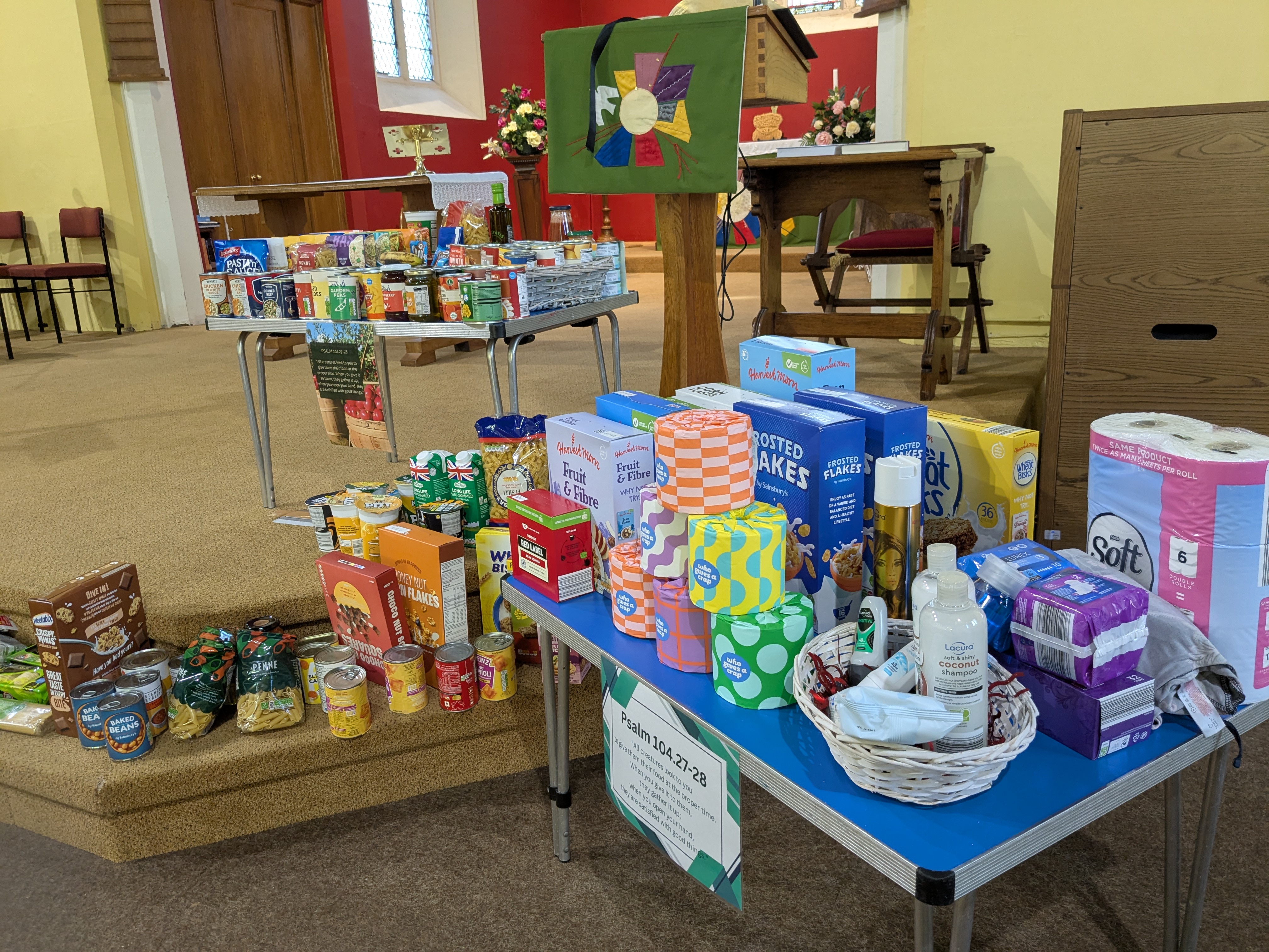 Tins and other harvest gifts on tables and at on the floor in front of the altar at Lye church