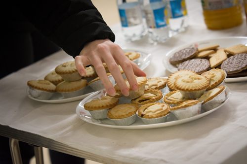 A hand takes a mince pie from a plate full on a table.