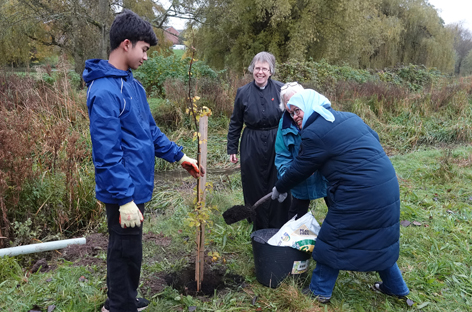 Catherine, Yvonne and Munirah put earth on the new tree as Munirah's son holds it in place