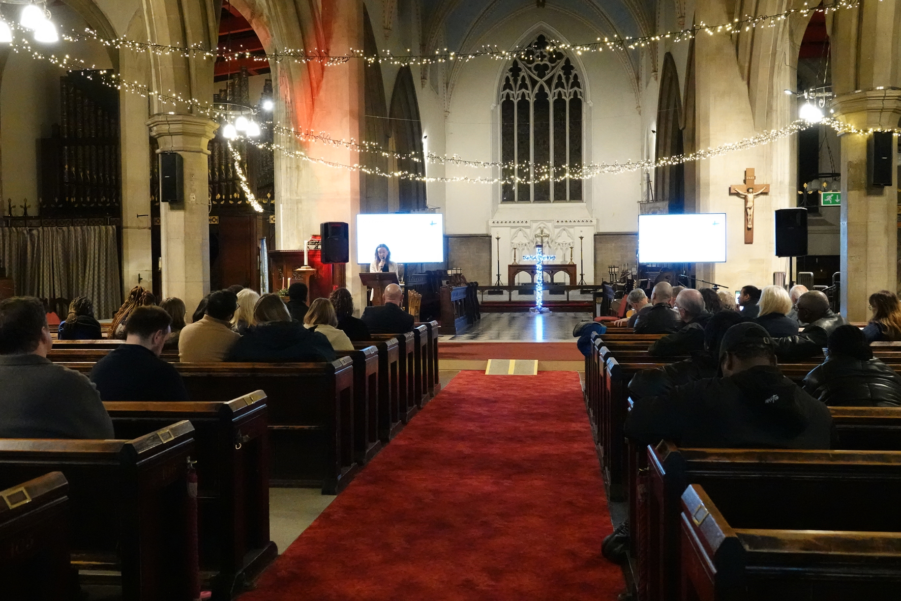 A view of St Stephen's church looking to the altar as people sit in pews listening to a speaker at the front.