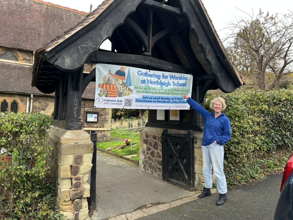 A lady pointing to a sign outside St Peter's church which explains that worship is in the school hall