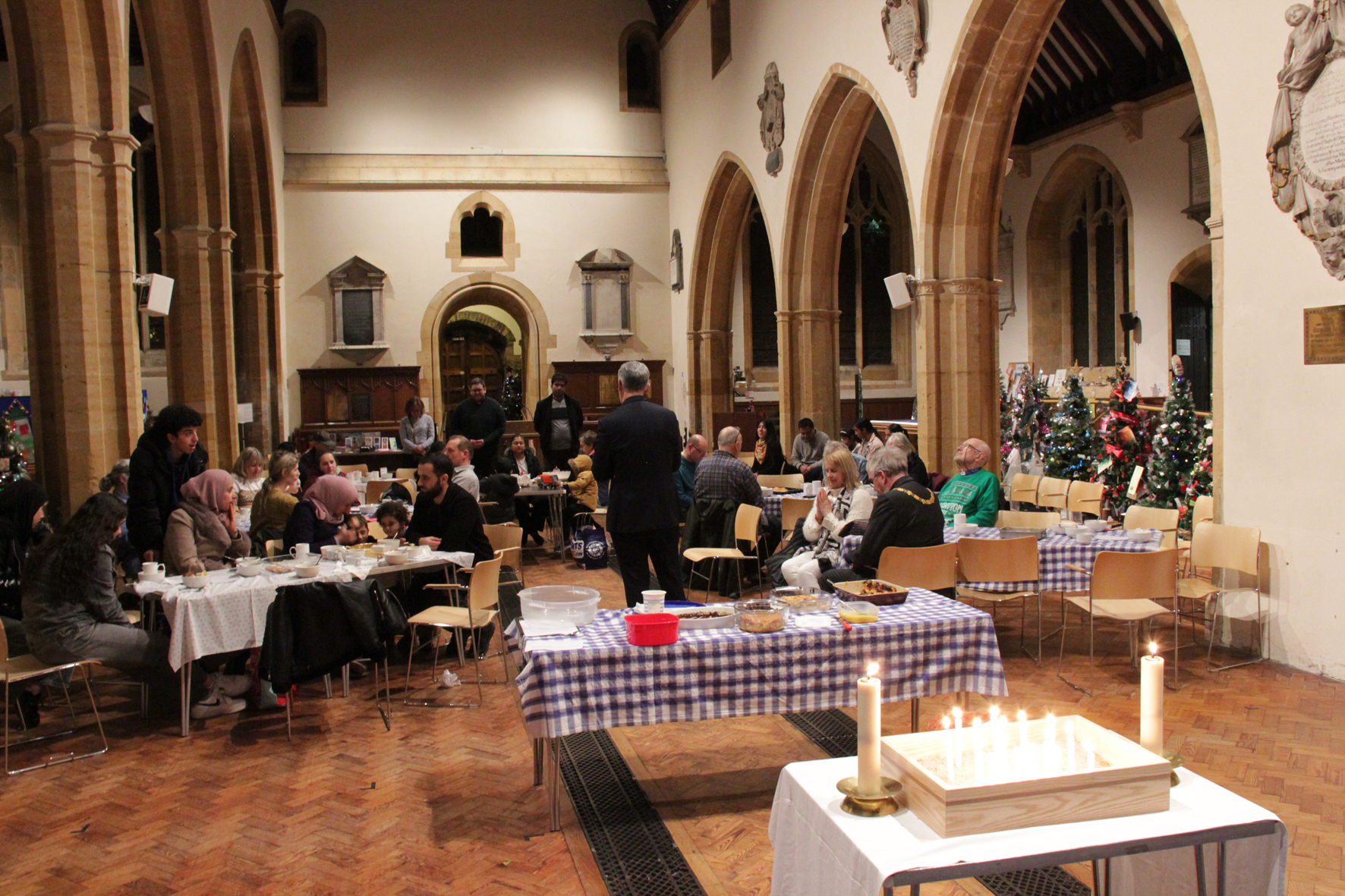 A view looking towards the front door of All Saints Church as Bishop Martin talks to people sitting around tables. In the foreground is a series of lit candles in sand.