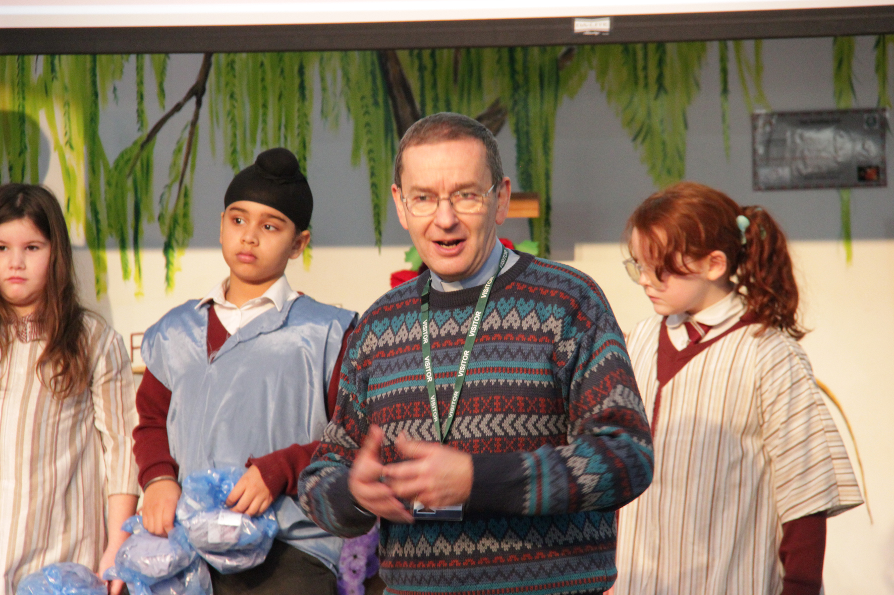 Vicar David Hildred stands in front of two children while talking at a school assembly