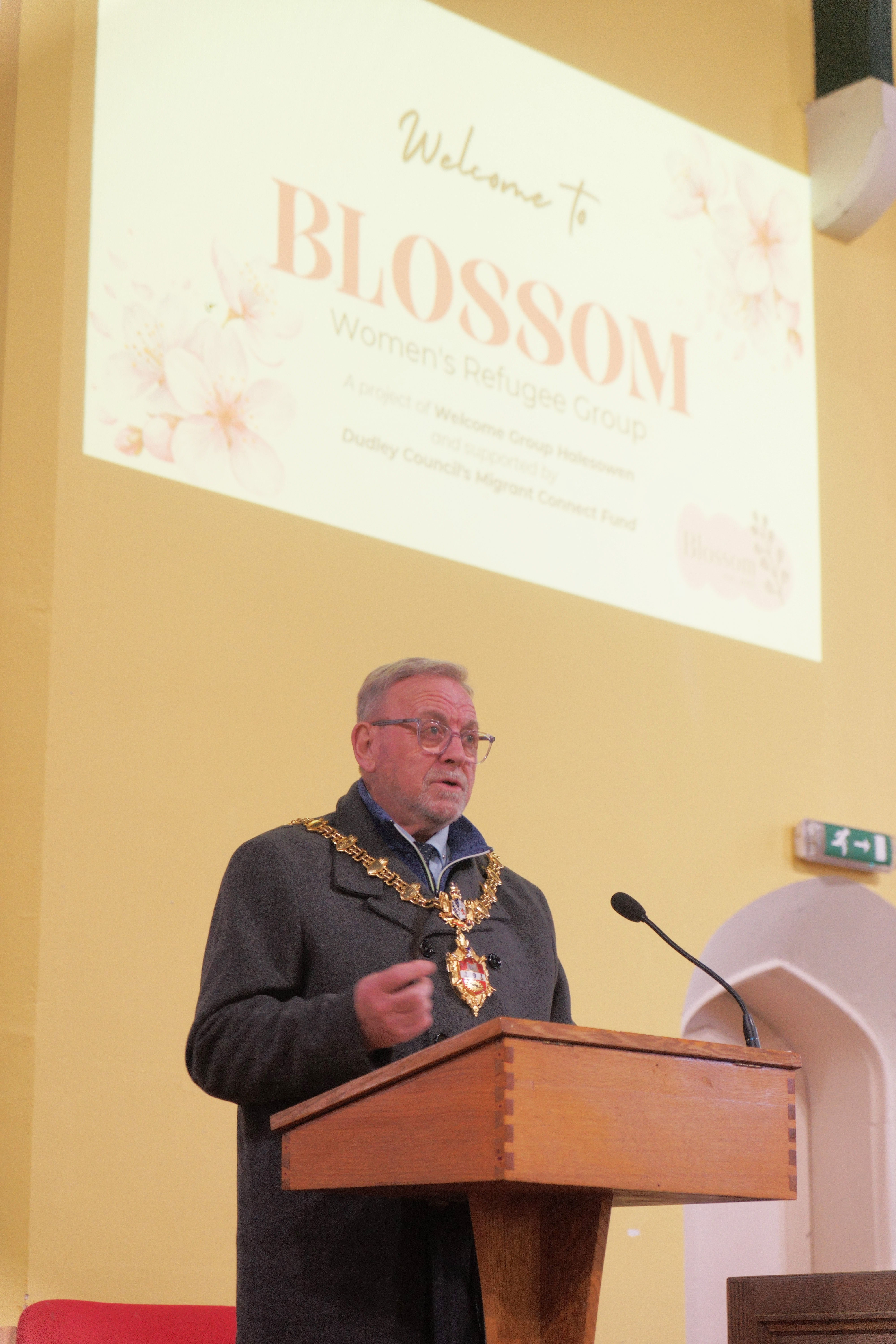 Mayor of Dudley standing in front of a big screen which says welcome to Blossom