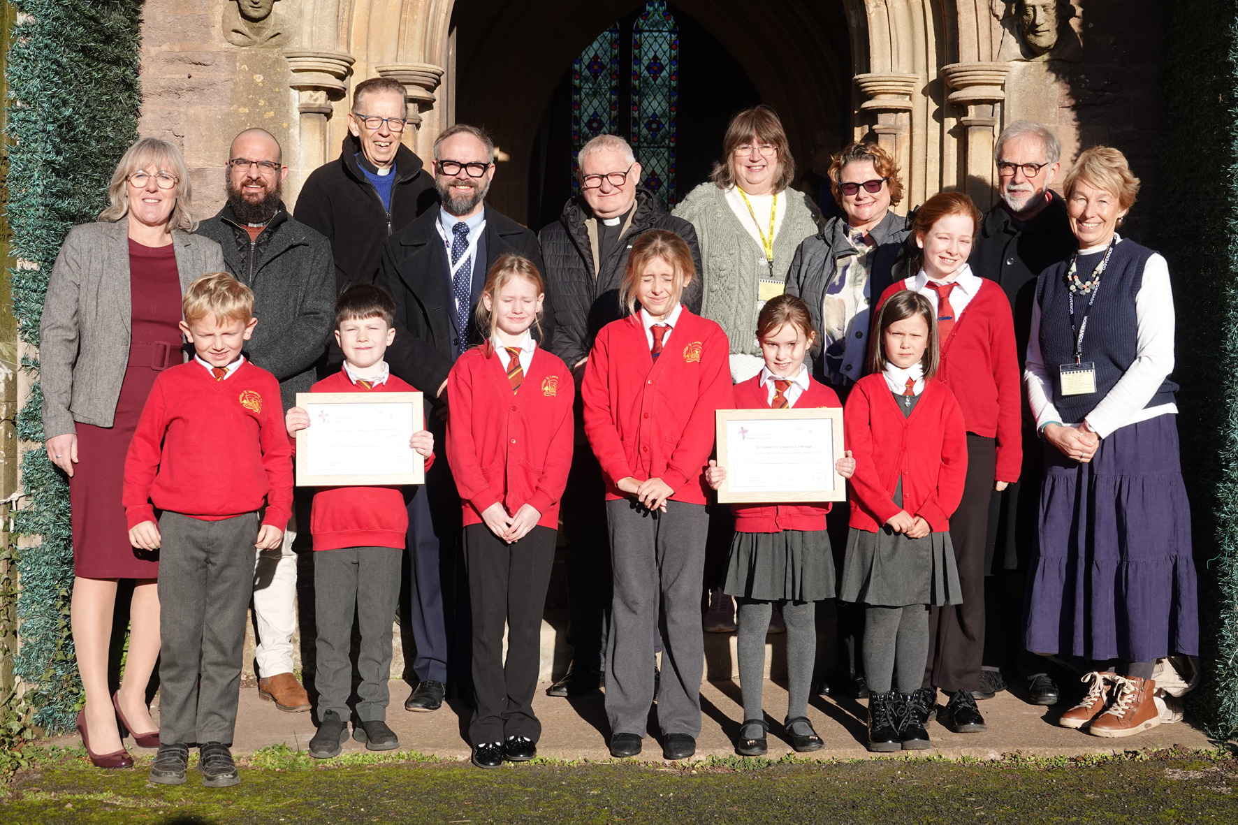 Pupils and staff from Lindridge school along with church representatives standing in front of the church doors holding two award certificates