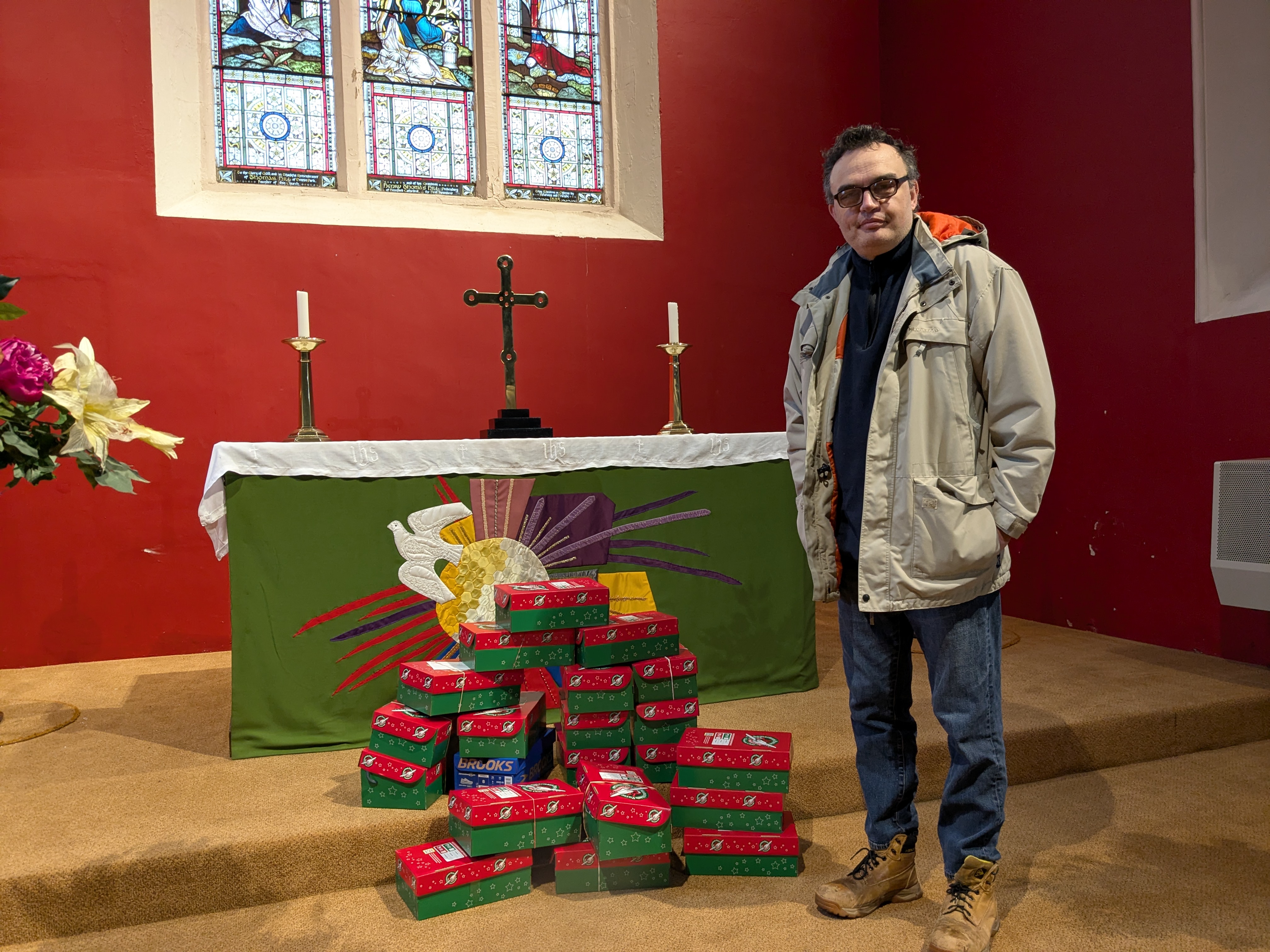 Congregation member David standing with a pile of Operation Child shoeboxes in front of the altar in Lye