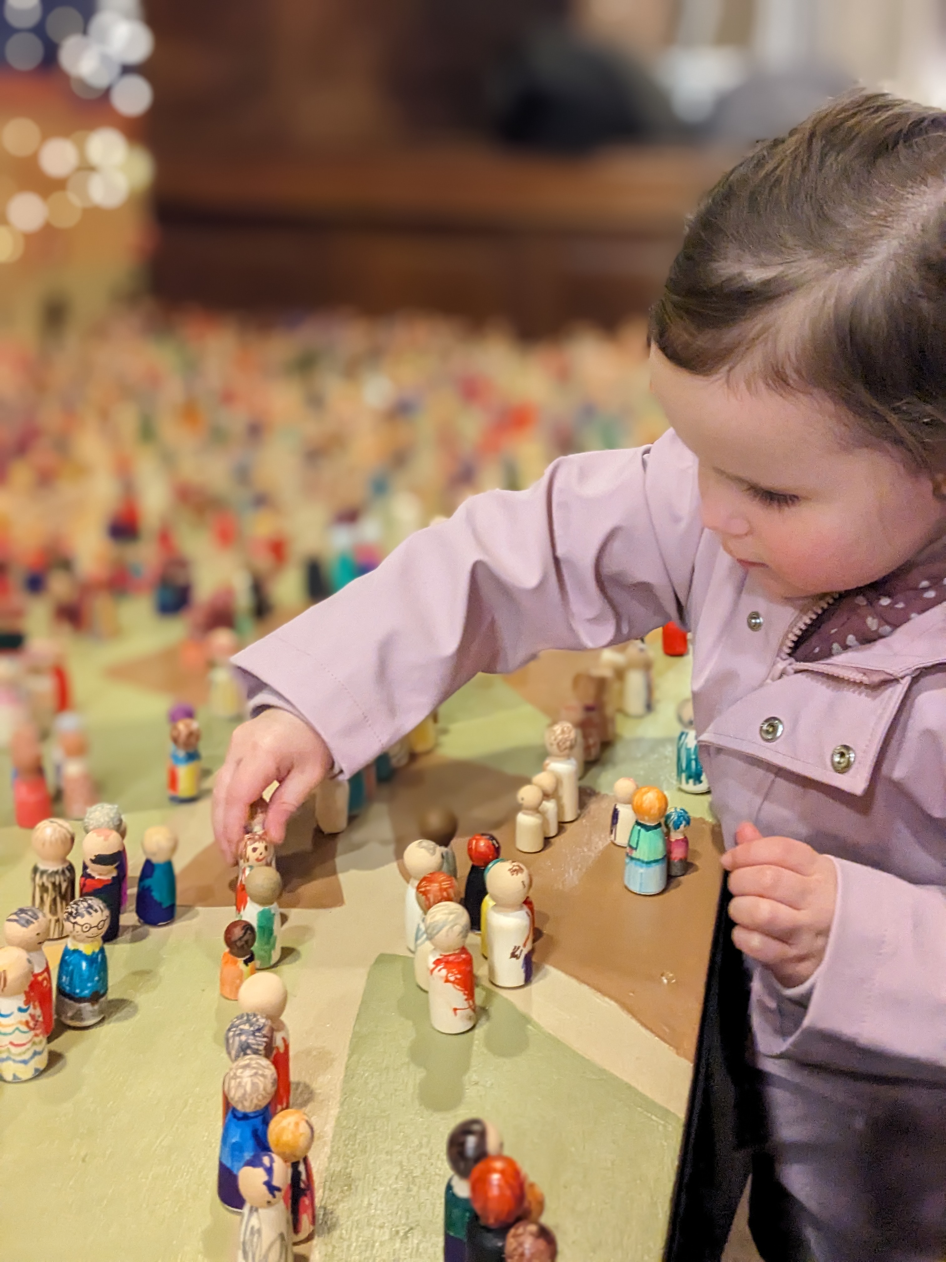 A toddler places a peg doll onto a table packed with other peg dolls