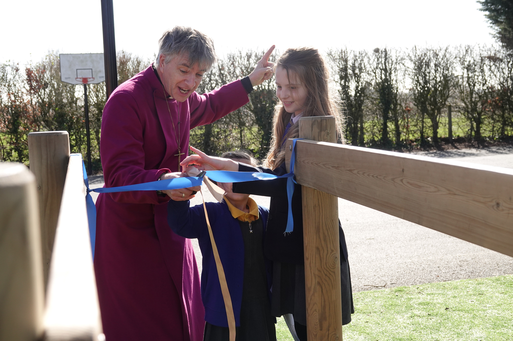 Bishop Hugh cuts a ribbon with the help of two students