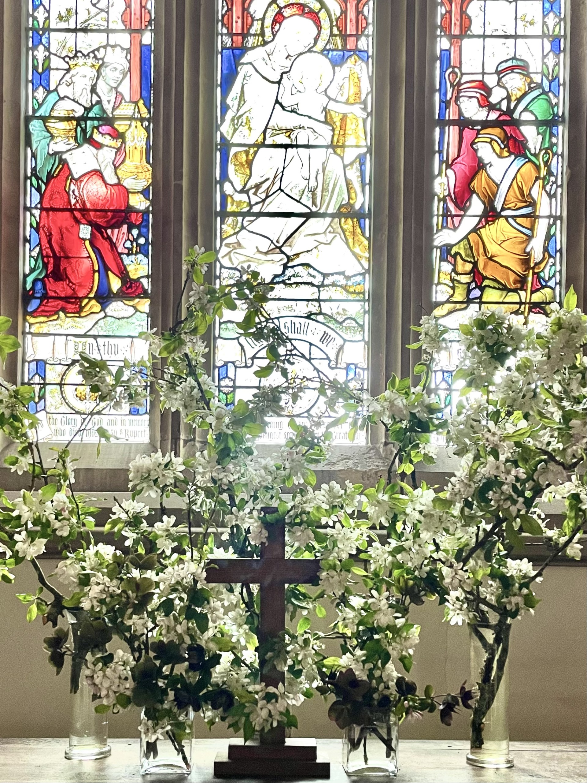 Display of white flowers in small jars on an altar with a cross in the foreground