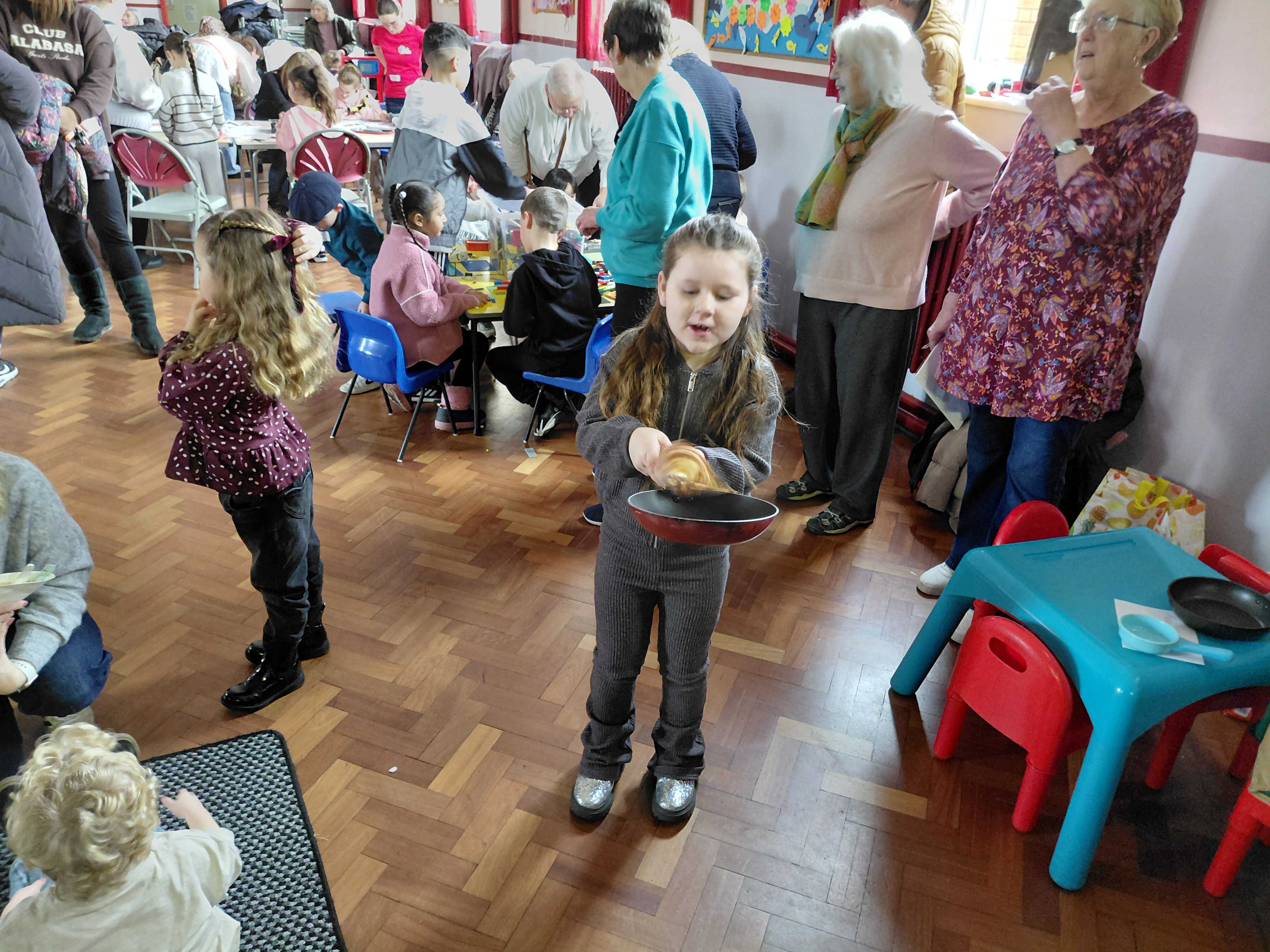 A girl tosses a pancake with other people in the background