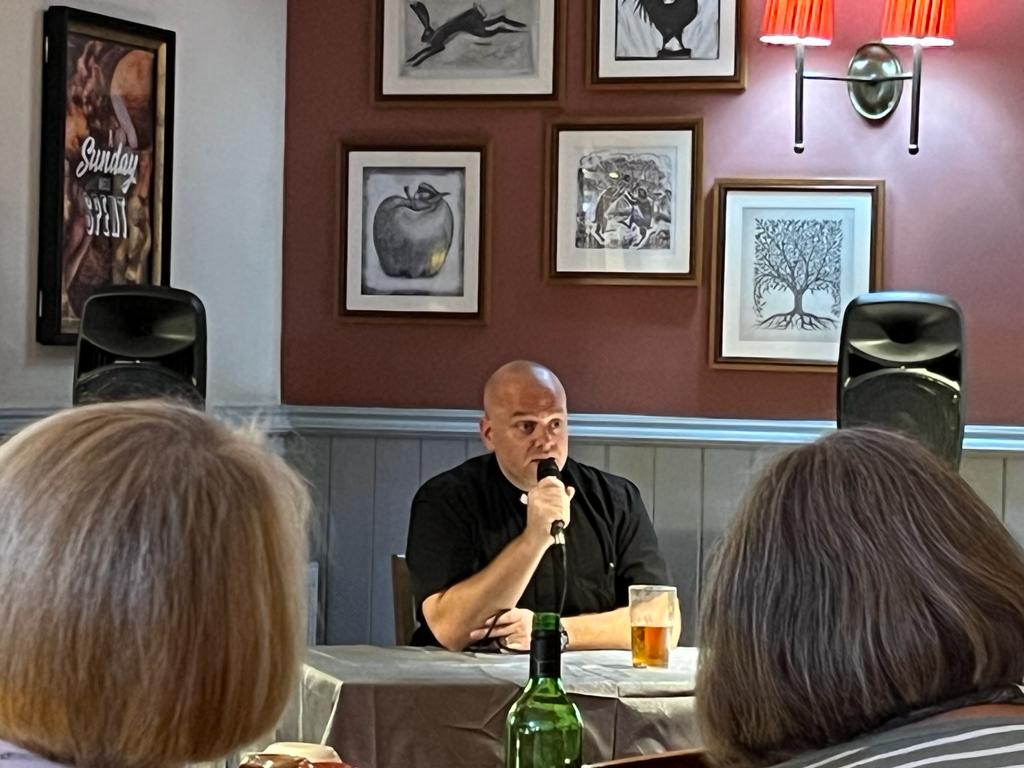 Shaun Armstrong sitting answering questions using a microphone with a pint in front of him