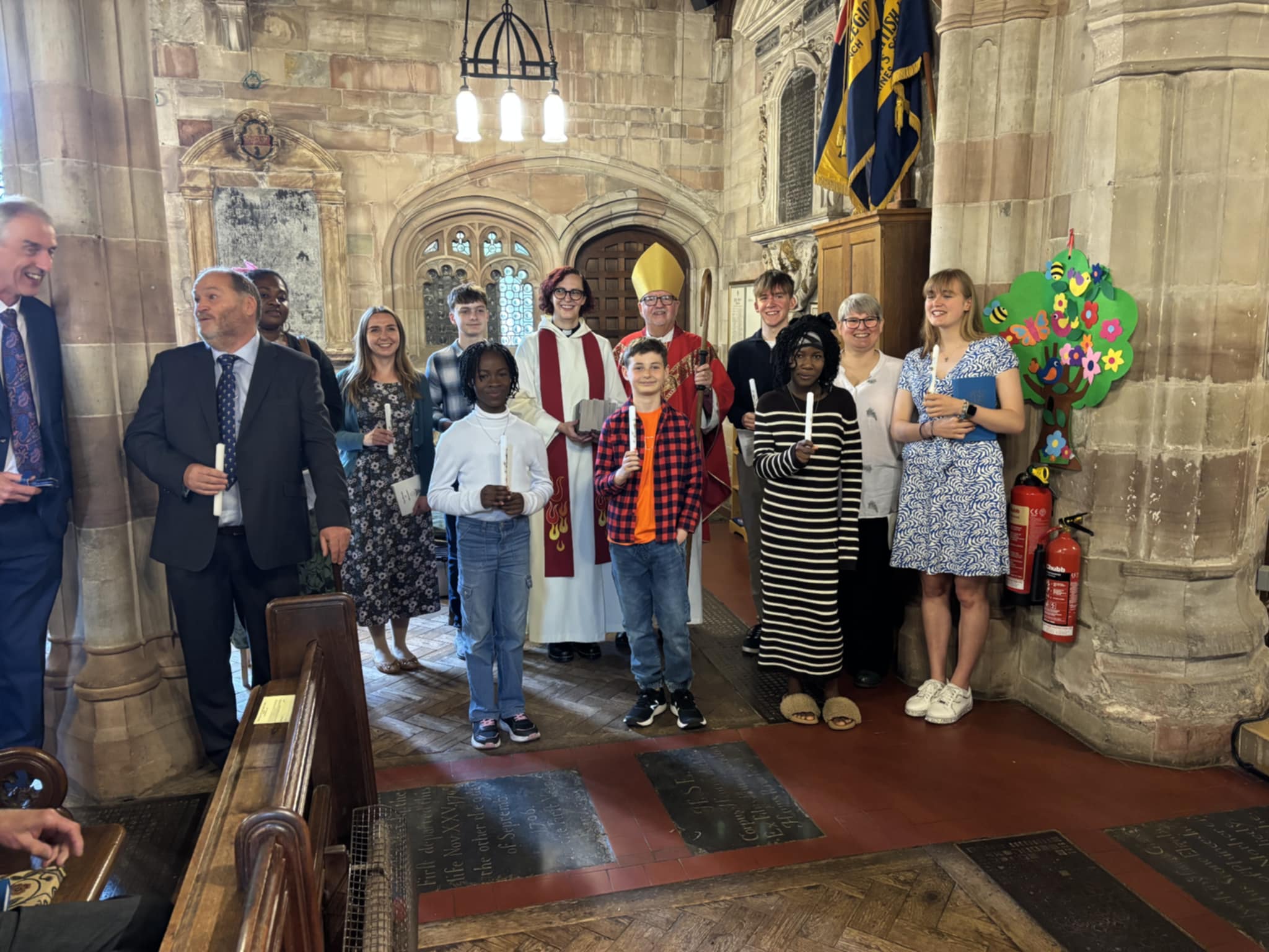 Confirmation candidates holding candles and standing with Bishop Alan and Revd Sarah in Claines church
