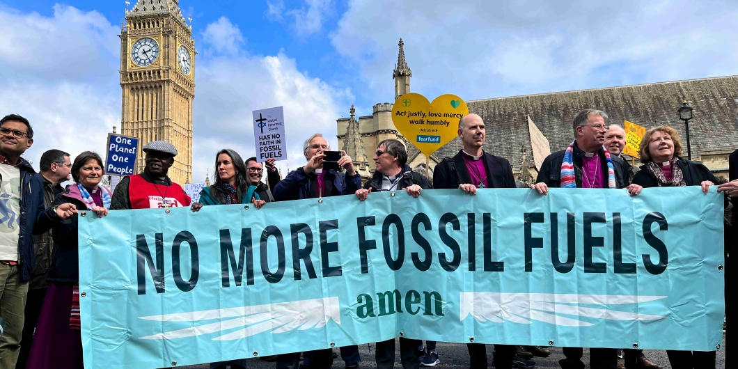 Group of people protesting outside Parliament with a no more fossil fuels banner