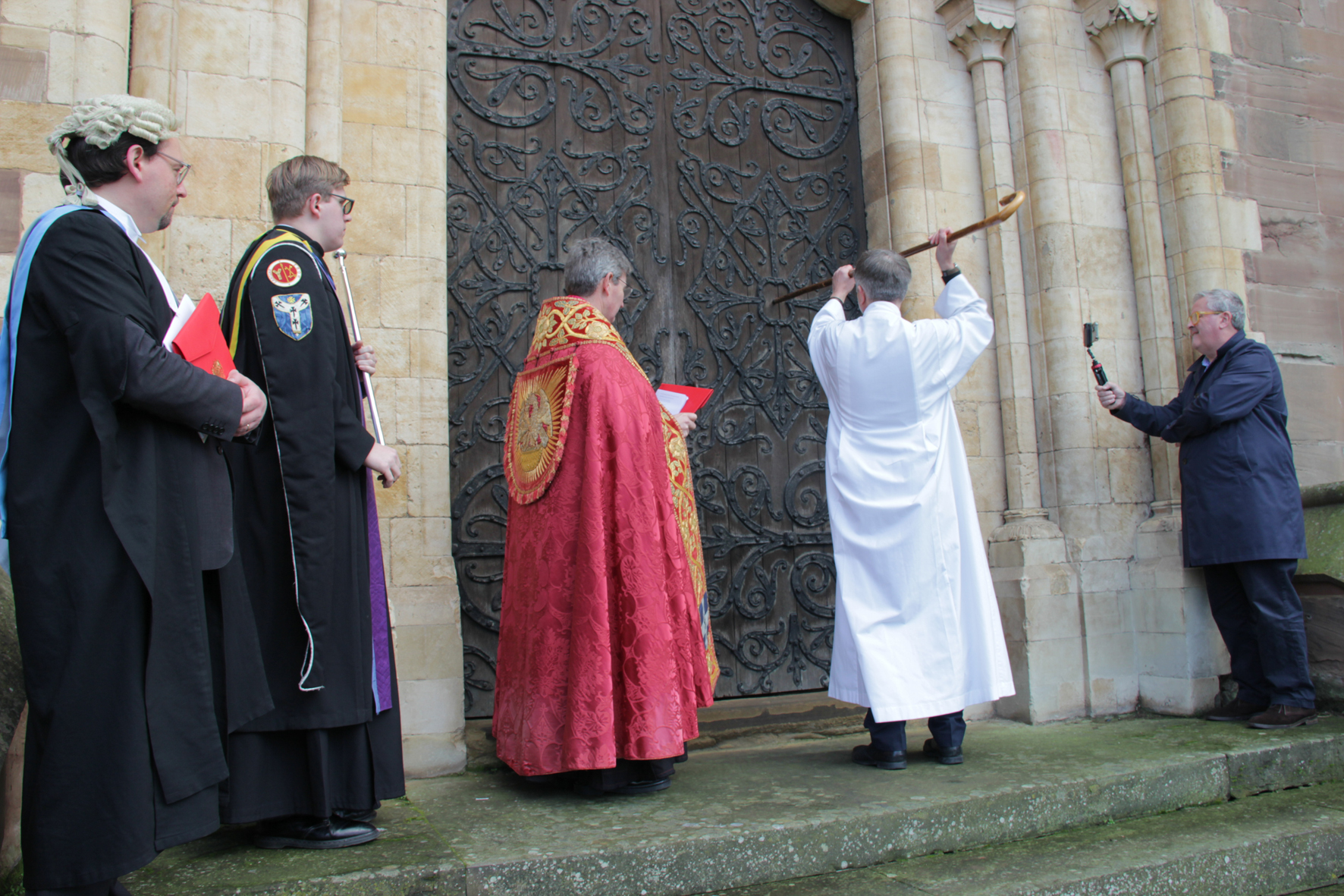 Bishop Hugh banging on the door of the Cathedral being watched by representatives from Canterbury