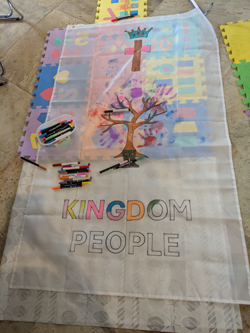 Partly coloured in flag with a tree, cross, crown and 'kingdom people' on with some pens next to it.