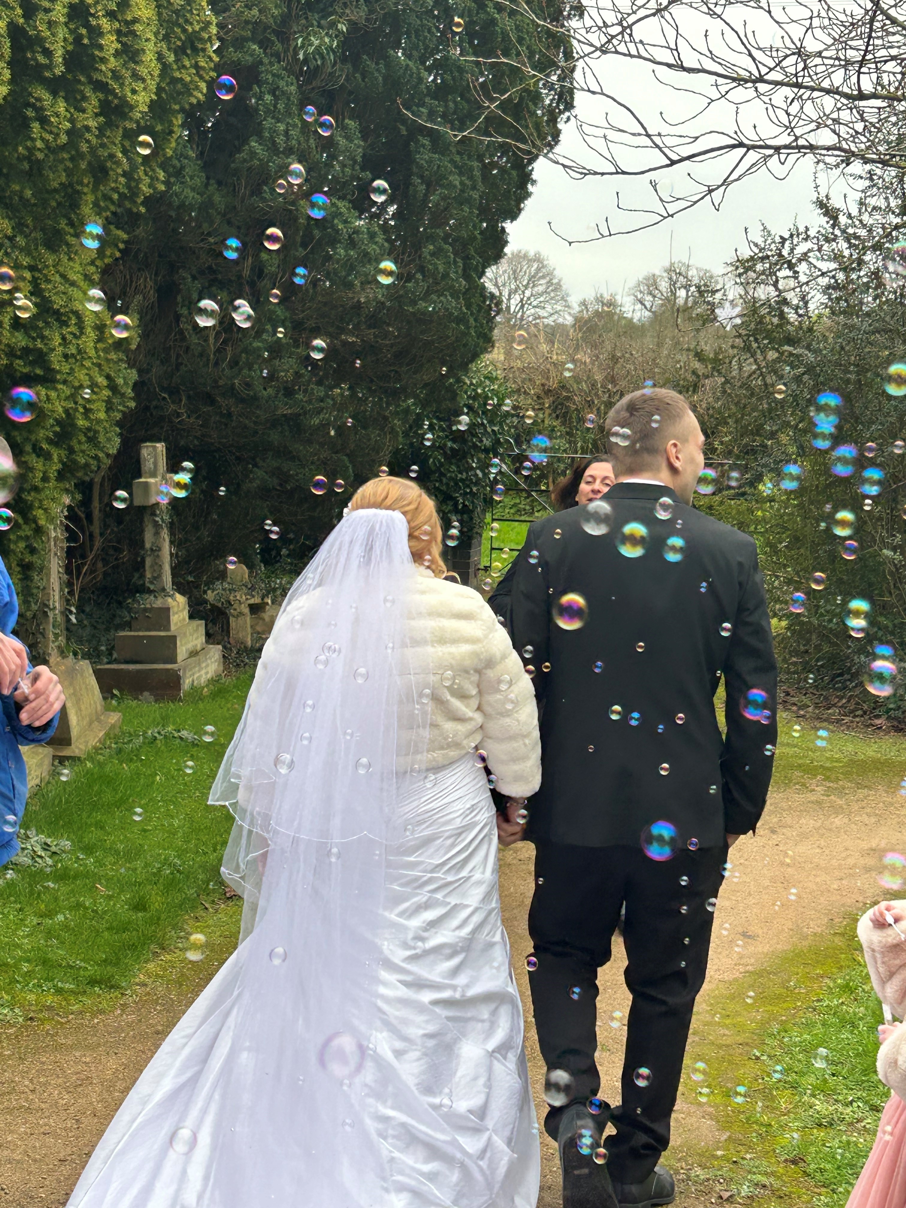 A wedding couple walking down a church path with bubbles