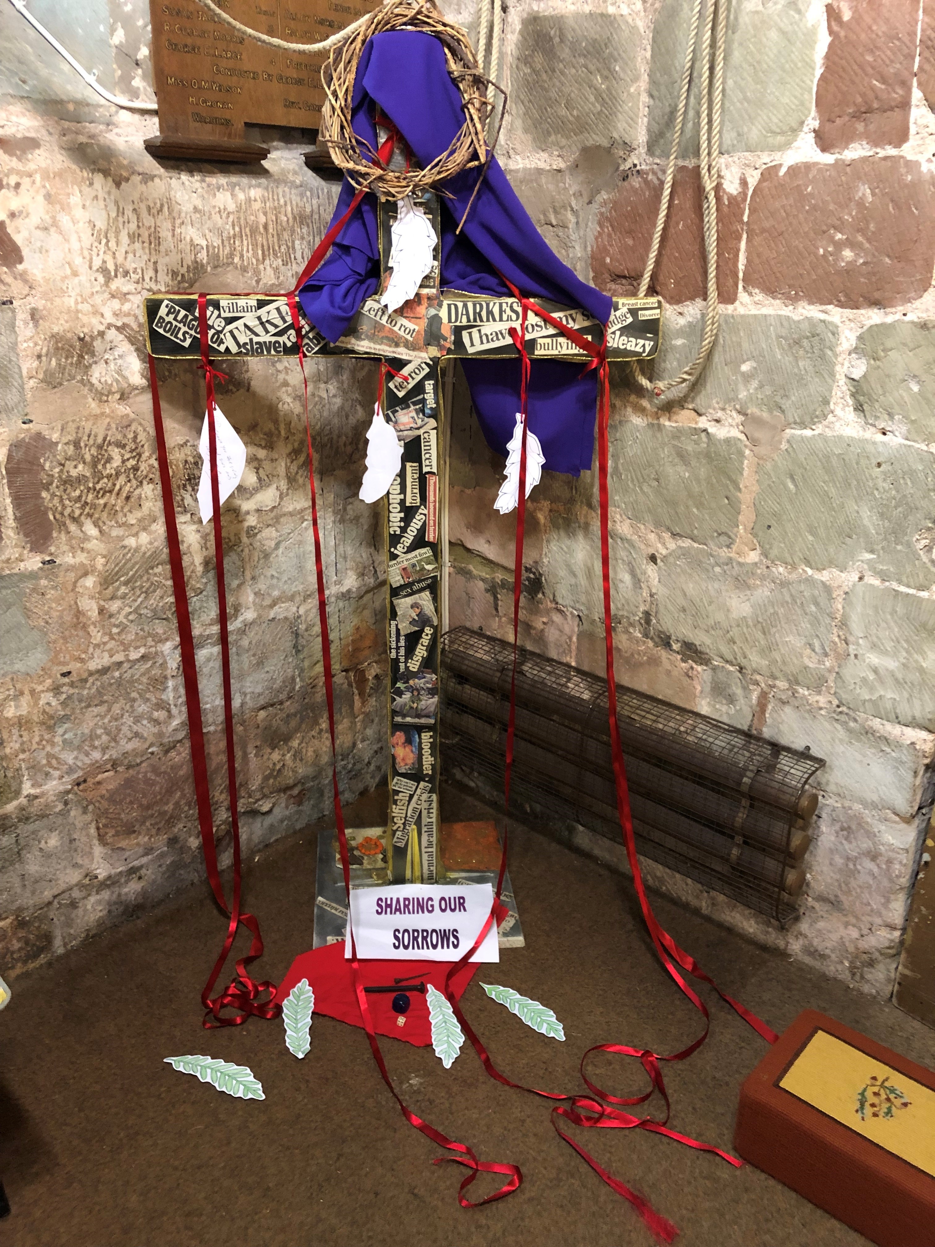 A large cross with different news headlines cut out and included and ribbons hanging down