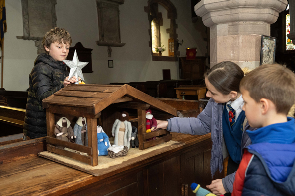children add knitted nativity characters to a stable and place the star on top