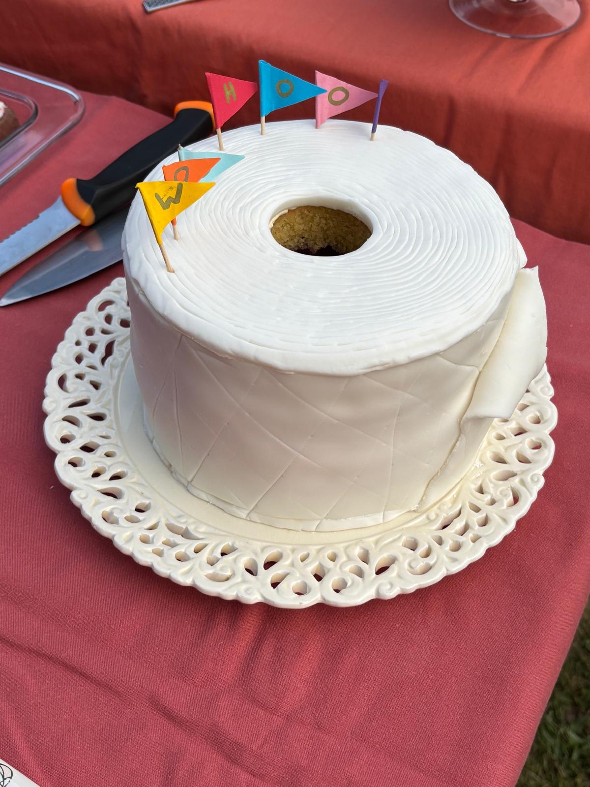 A cake covered in white icing to look like a full toilet roll with miniature flags in the top