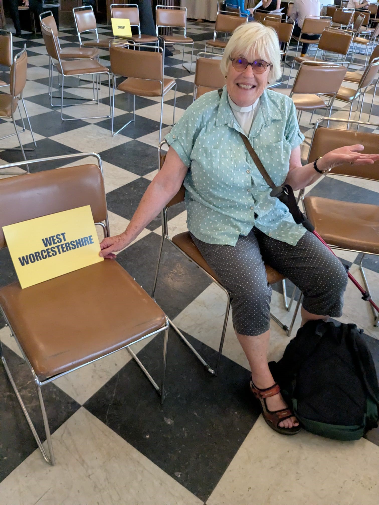 Sue Adeney sat on a chair next to another chair with a 'West Worcestershire' sign on.