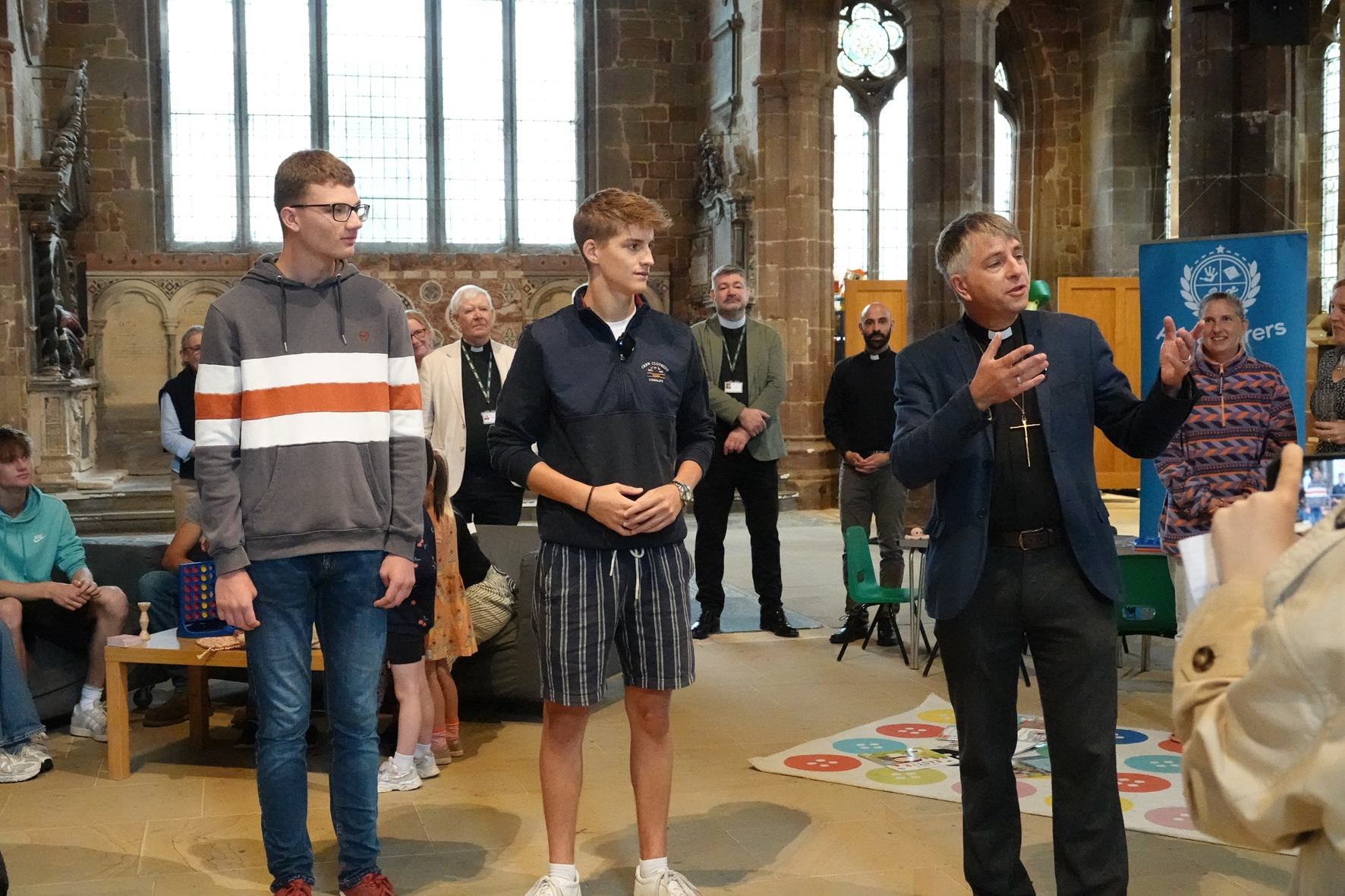 Bishop Hugh standing next to two teenage boys speaking to people gathered