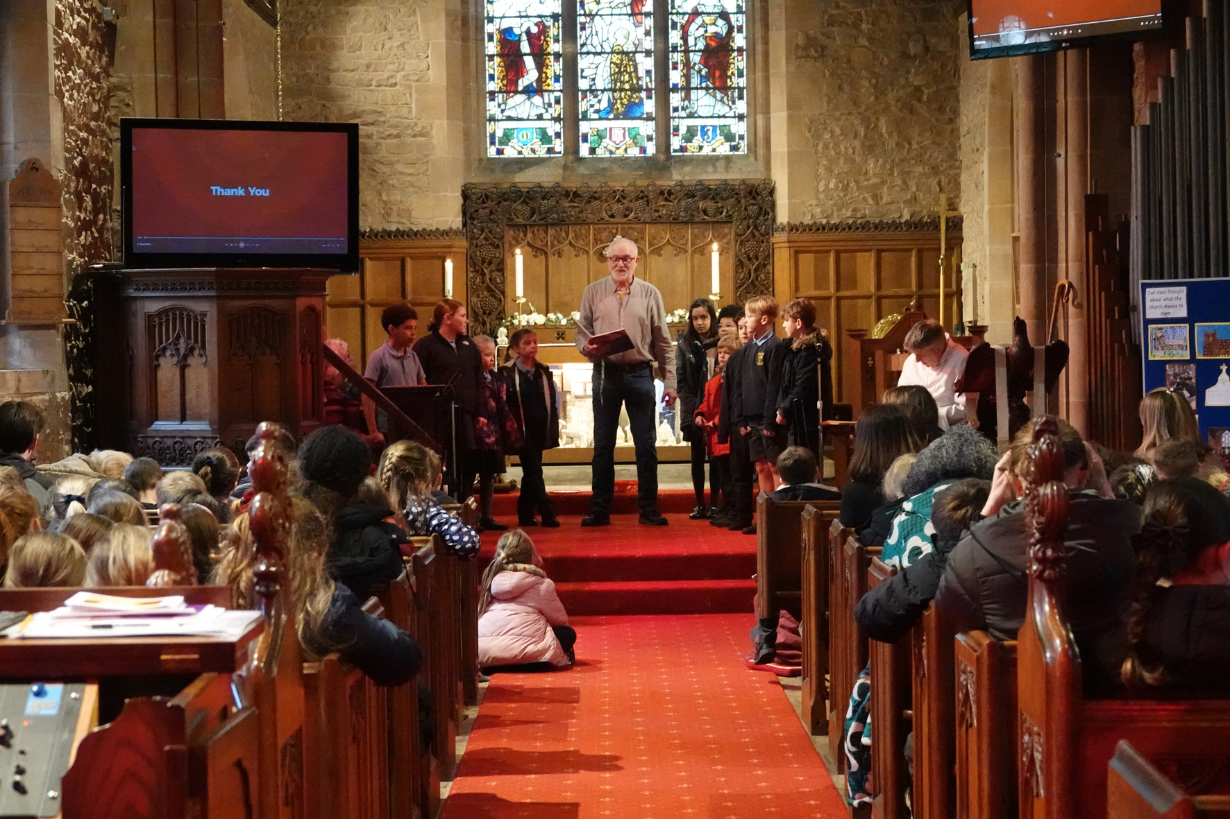 Ian Craigan stands at the front of Lower Broadheath church with a group of children performing an Open the Book story being watched by the rest of Broadheath school