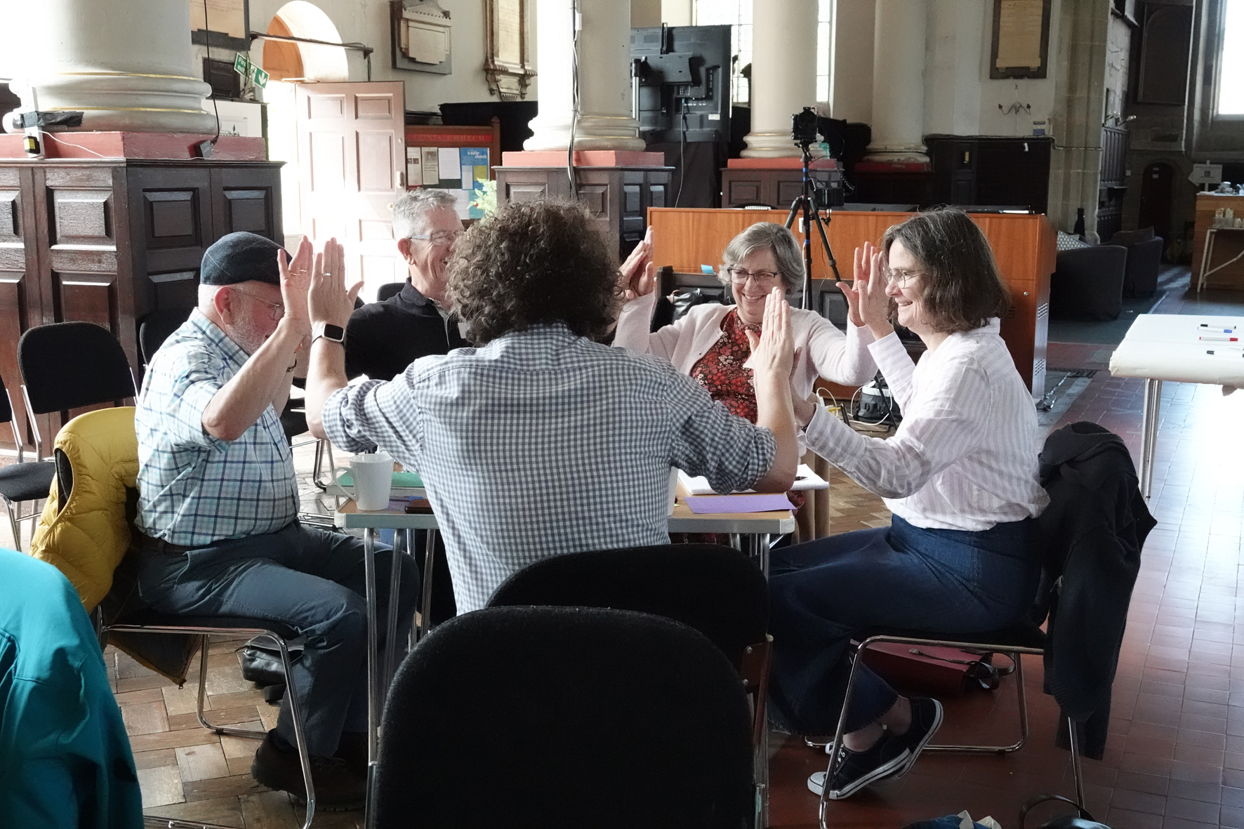 A group of mission accompaniers sat around a table doing a group high 5