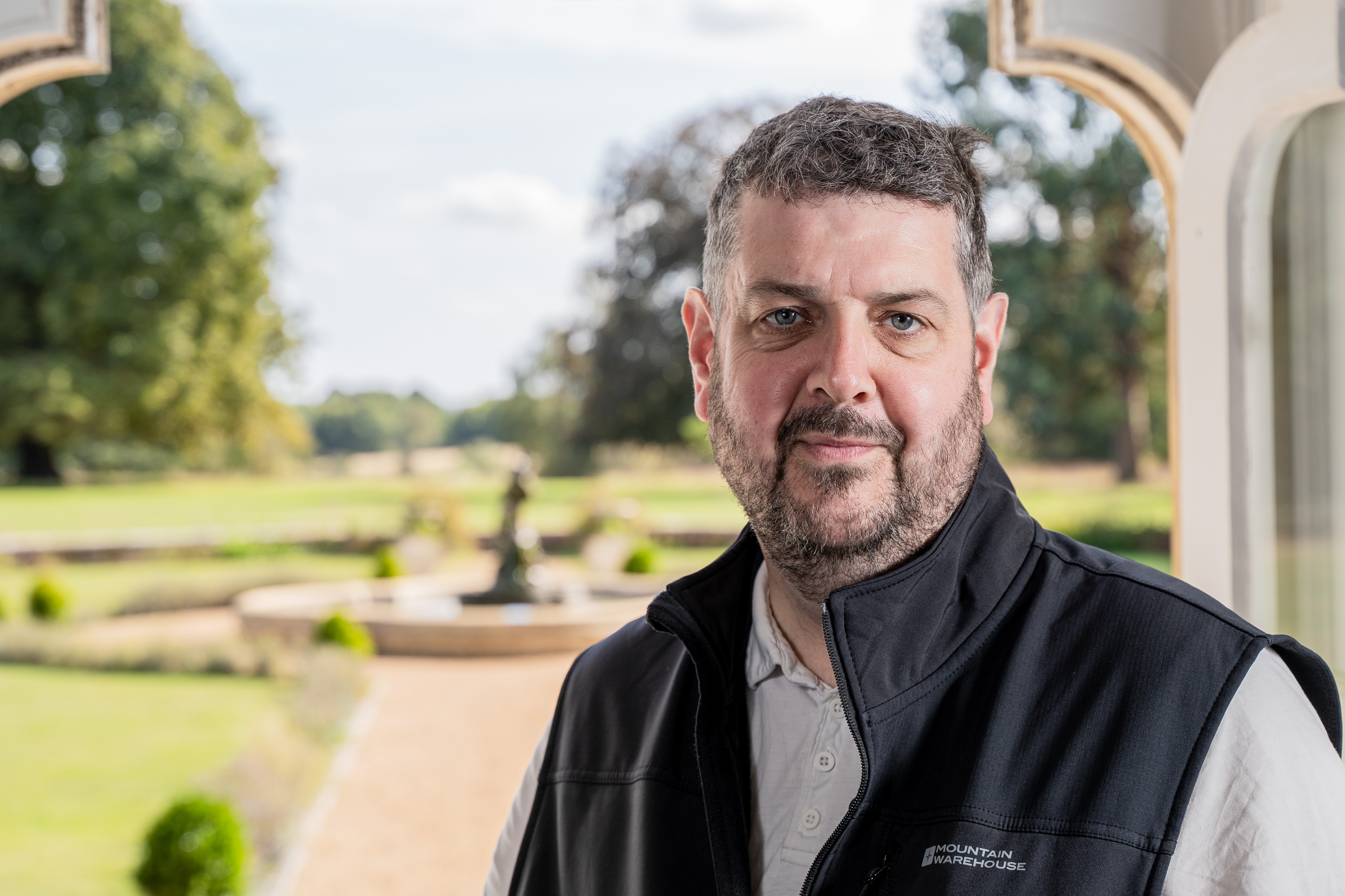Head and shoulders photo of Glenn Reading standing in front of an open door leading out into a garden