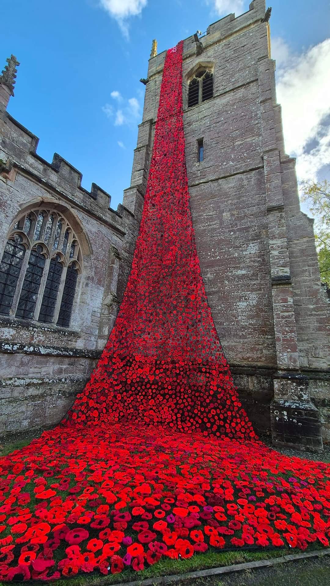 Knitted Poppies cascading down the tower of Inkberrow church and spreading out on the ground below.