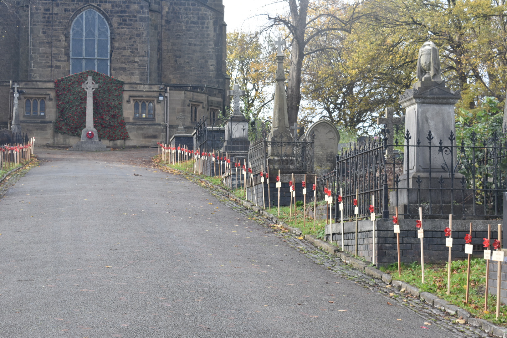 Poppies on crosses lining the path up to church and the war memorial with a net filled with poppies behind