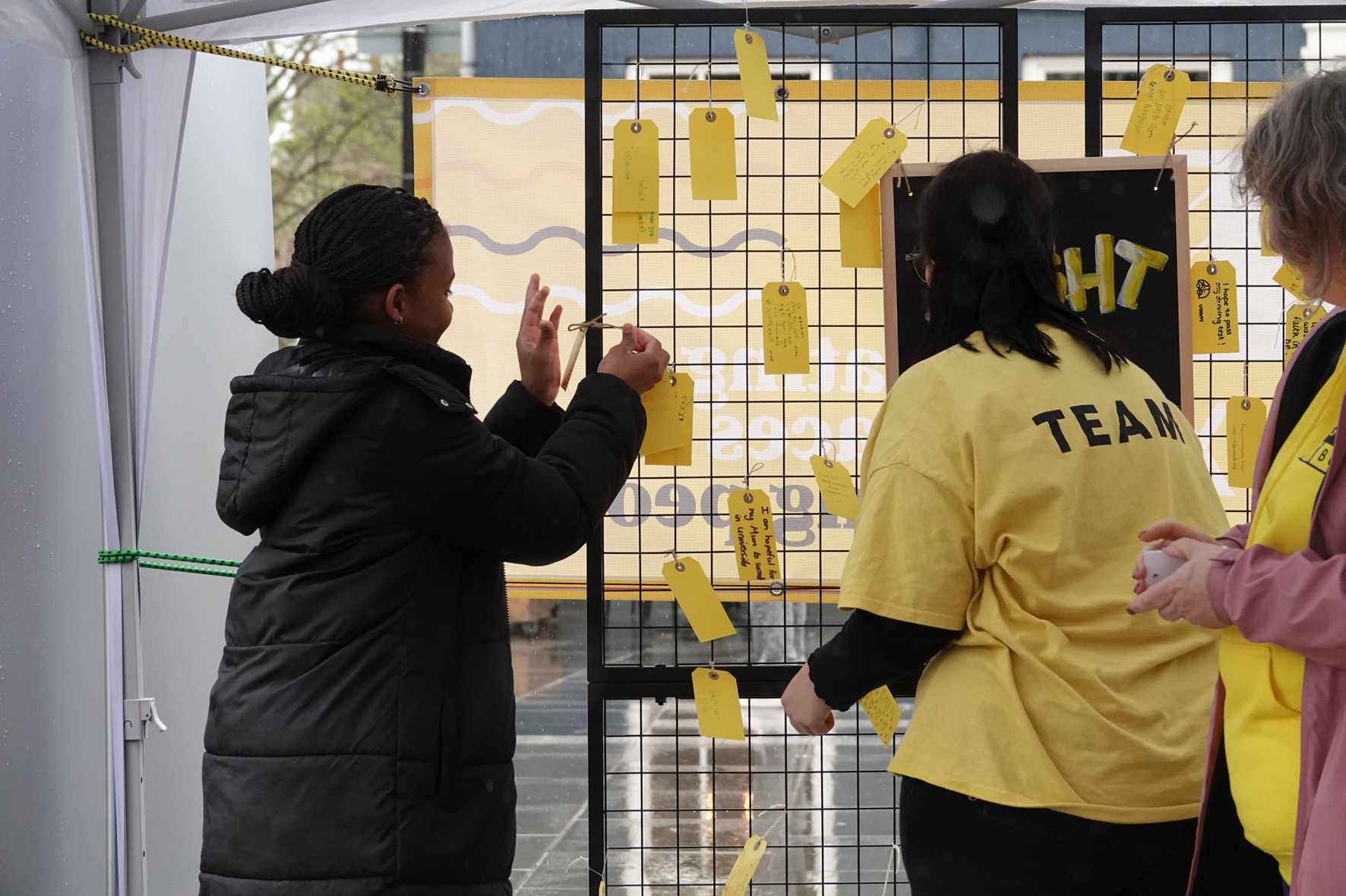 Girl puts a tag with a prayer on a prayer wall watched by a member of the Lighthouse team