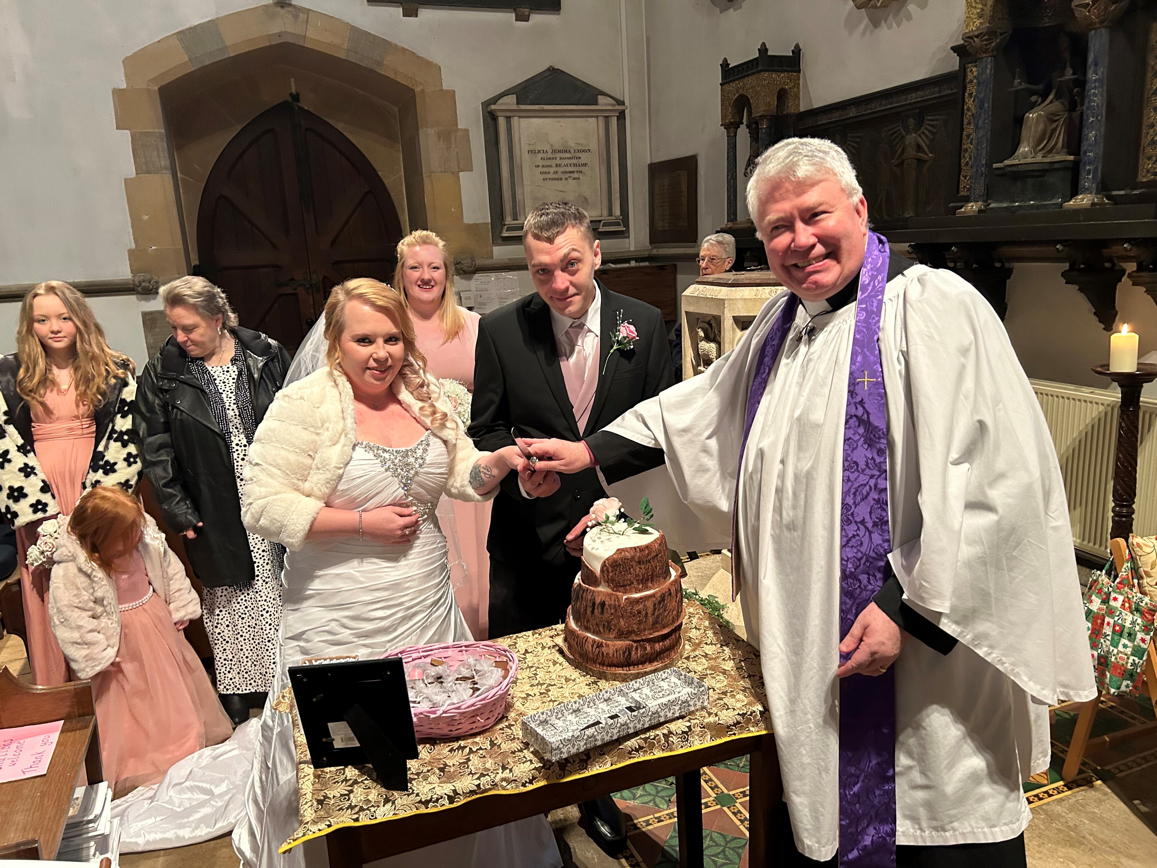 Vicar Gary Crellin with the couple as they prepare to cut their cake