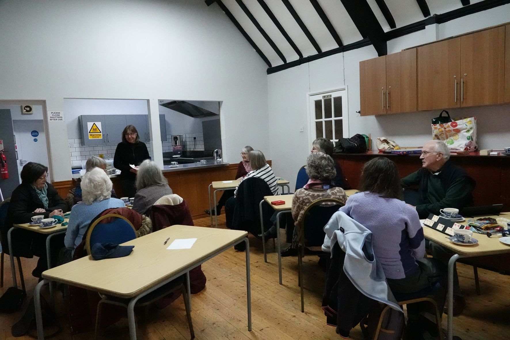 People sitting around tables listening to a person at the front of the room speaking