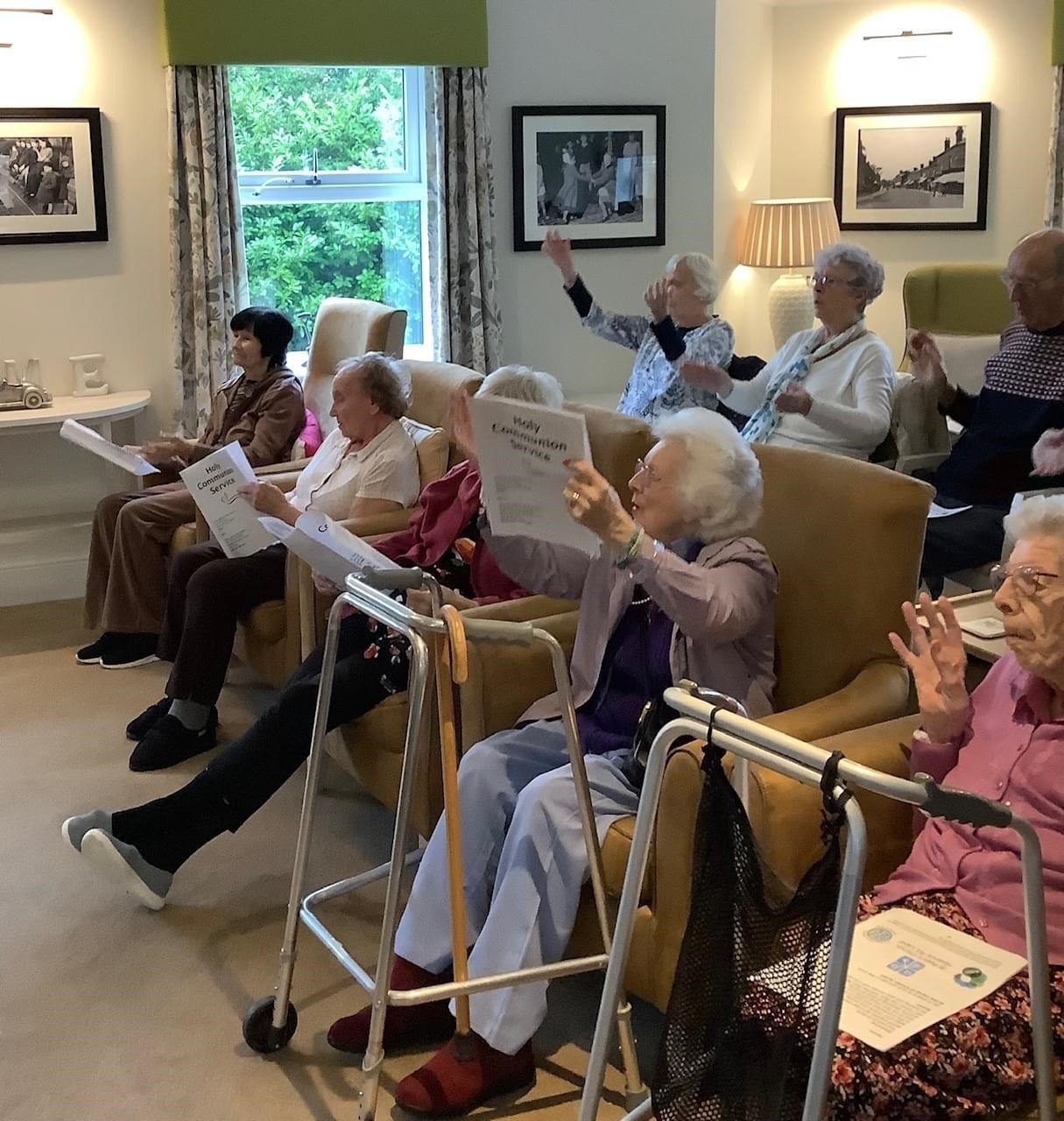 Residents of a care homes sitting in rows and raising their arms in worship