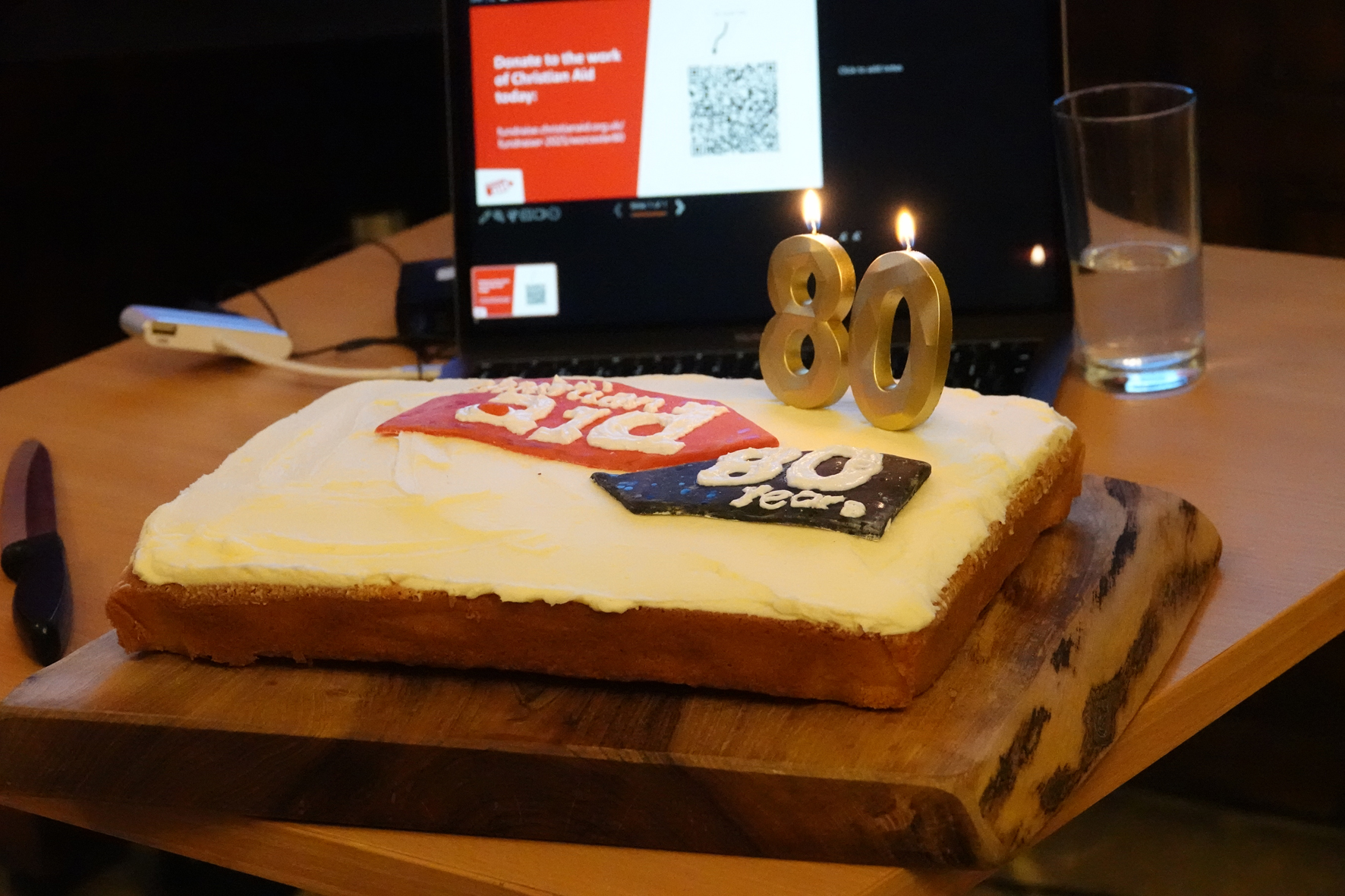 Rectangle cake with the Christian Aid logo iced on and candles saying 80.