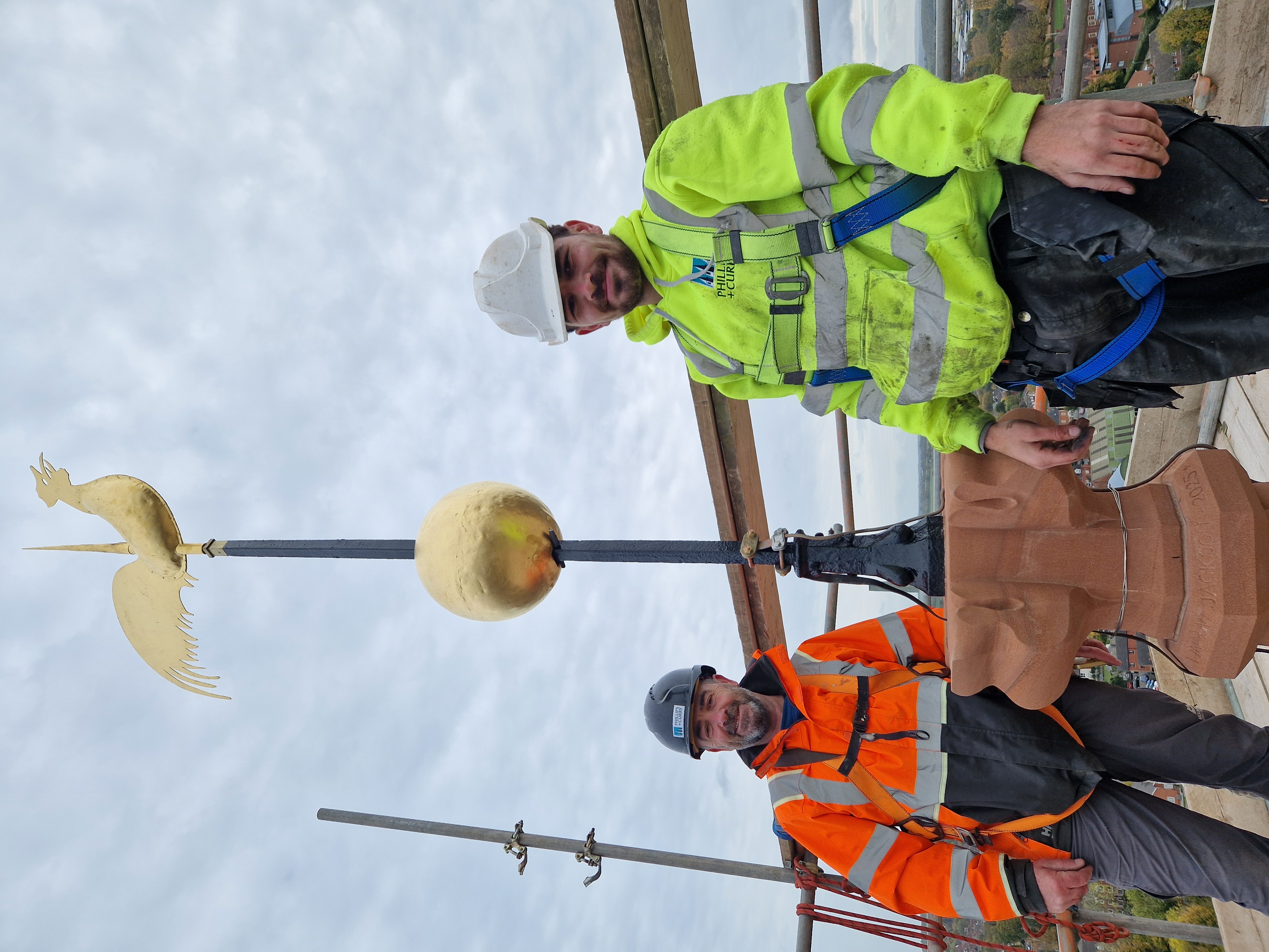 Two workmen stood at the top of st John's spire next to the newly fitted weathervane