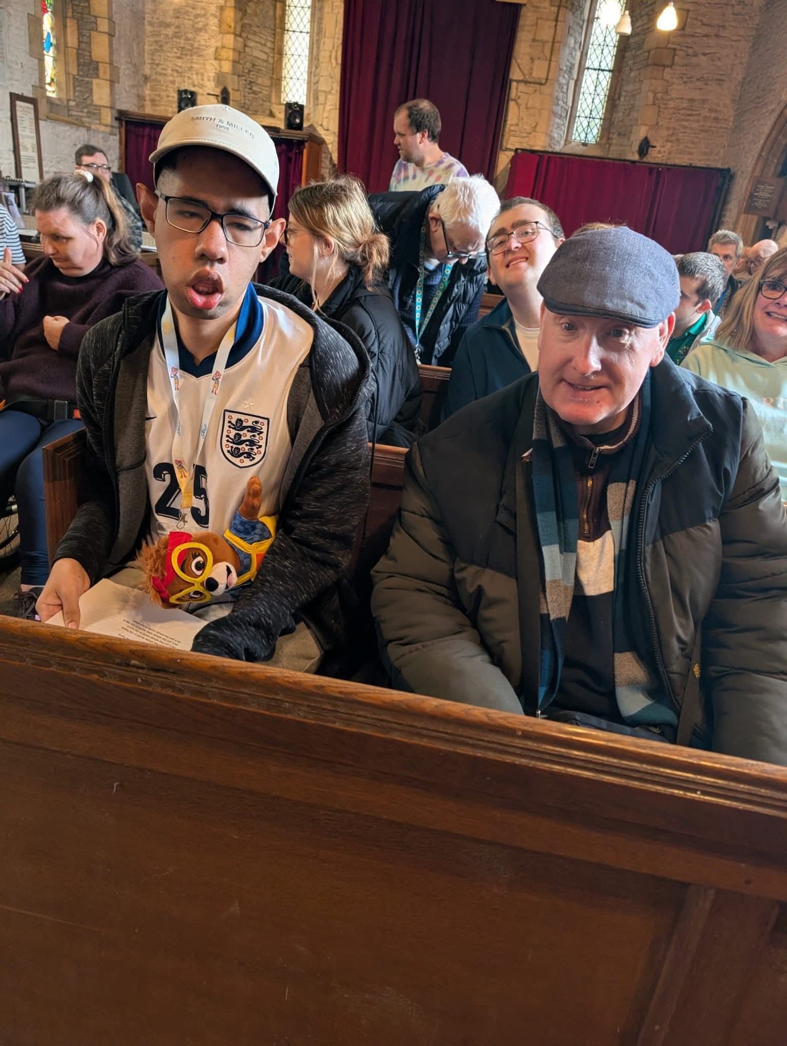 Two men sitting in church pews with a further congregation behind them