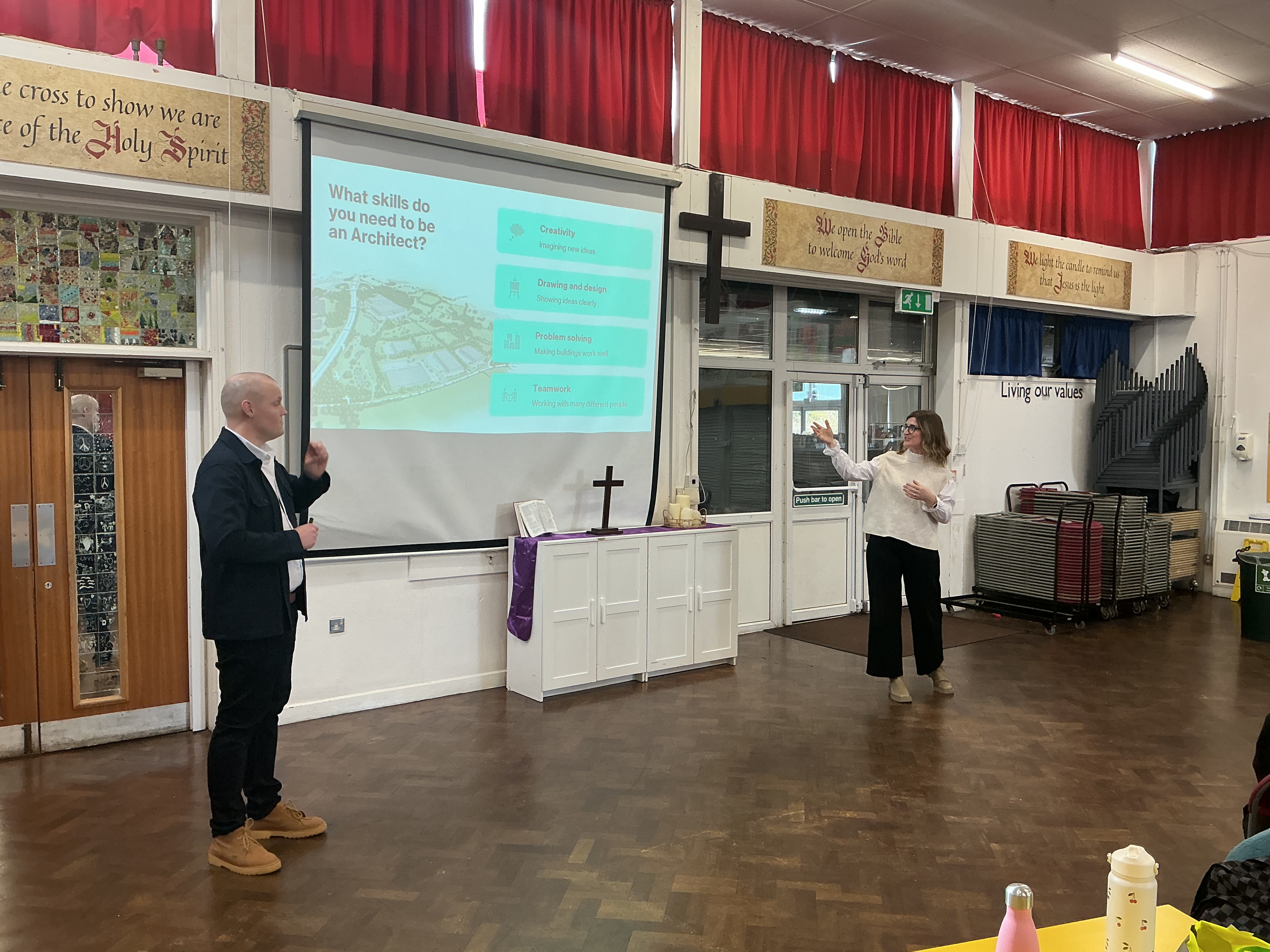 Two people stood in front of a screen with information about Architecture on in a school hall