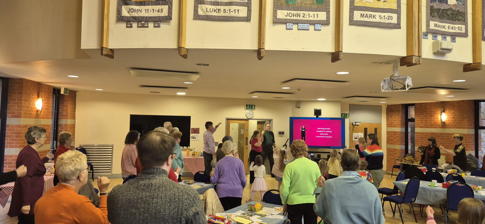 a view of the backs of people all looking at iSingPop song on a screen at the front of the room.
