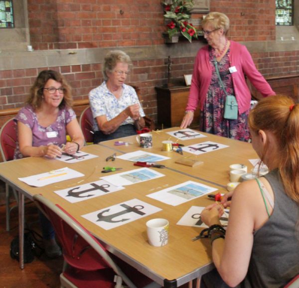 On one of the activity tables, participants bend wire with pliers into the shape of an anchor, whilst chatting to each other