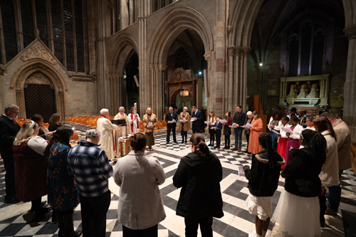 Confirmation candidates standing in a circle at the back of the cathedral before Bishop Martin baptises one candidate